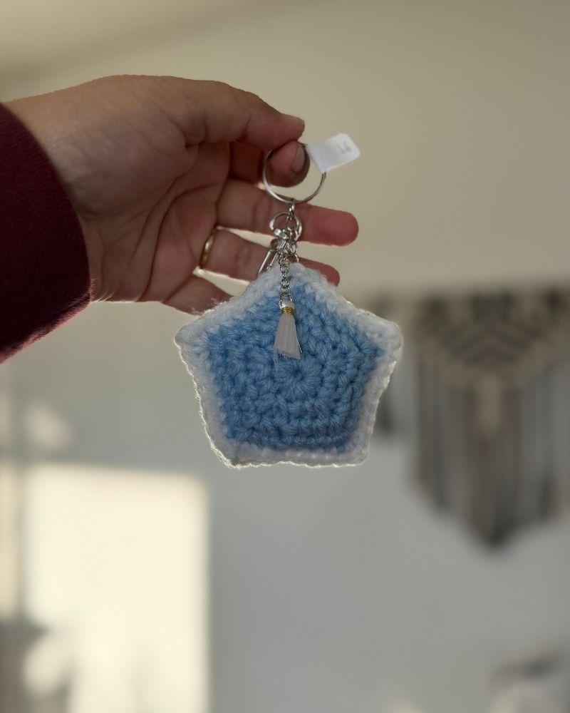 Hand holding a blue star-shaped keychain with a tag against a neutral background